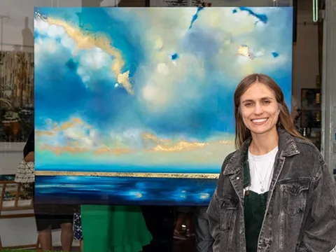 charlotte aiken stood infront of a blue and gold landscape painting